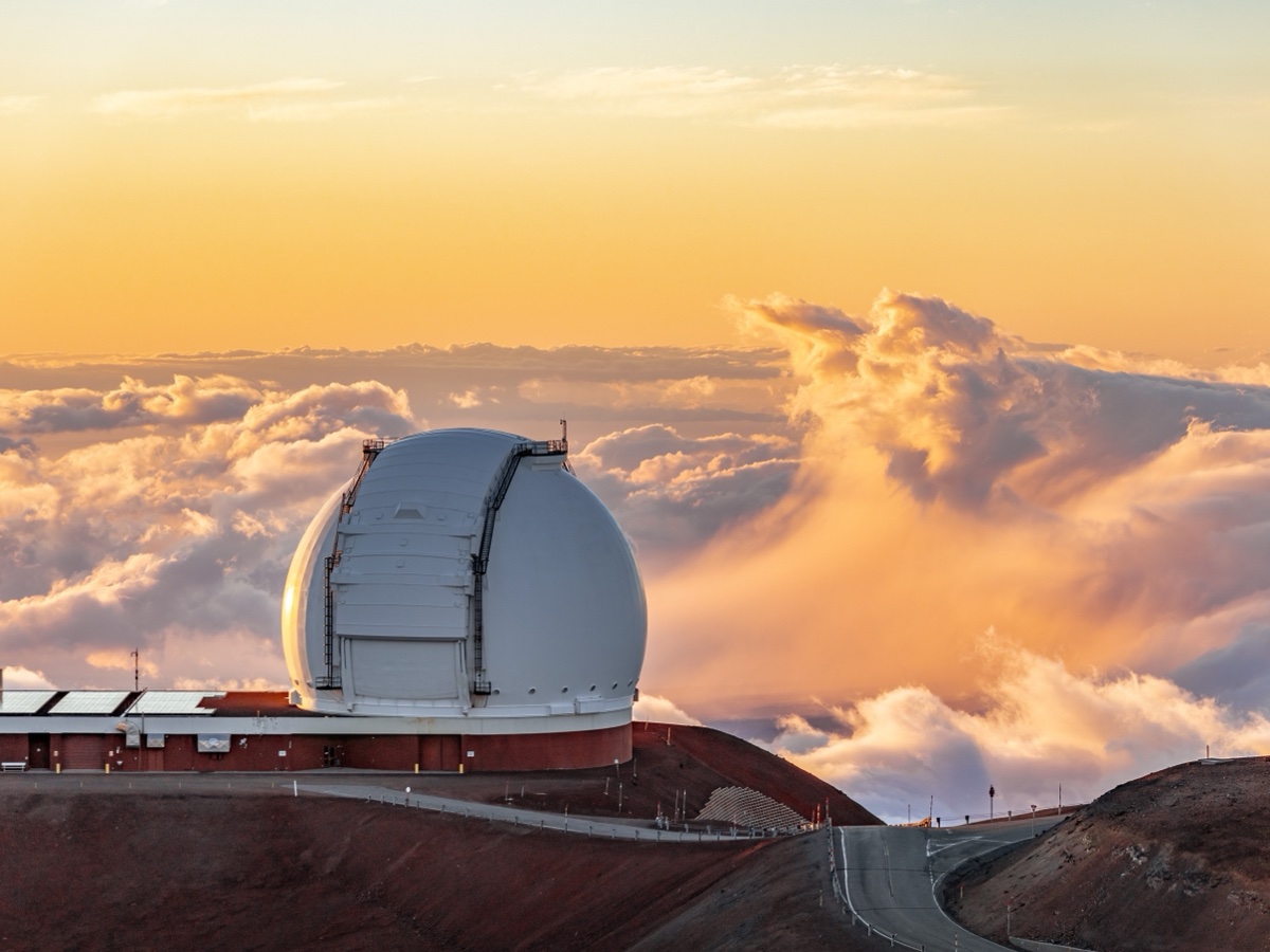 Dôme blanc d'un des deux télescopes de l'observatoire Keck au sommet du Maunakea, au-dessus d'une mer de nuages dorée au coucher du soleil