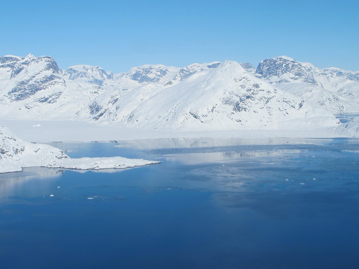 Fjord du sud-est du Groenland vu d’avion, montagnes enneigées et eau sombre parsemée de glace