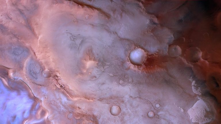 Vue verticale d'une région glacée près du pôle Sud de Mars, dans des tons violets, roses et rouges, avec des cratères, une falaise et un glacier bleuté à gauche