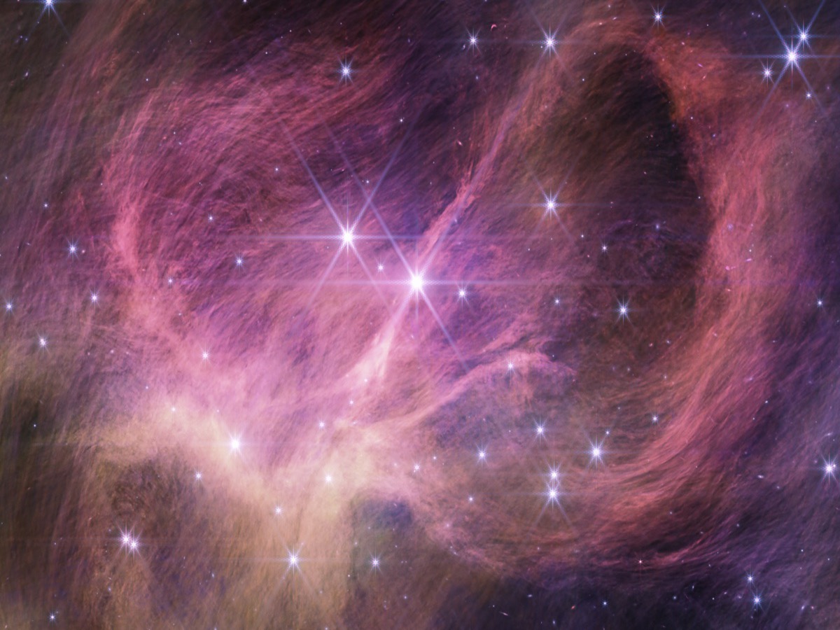 Nuages de gaz et de poussières aux teintes roses et violettes formant de grandes volutes, parsemés d'étoiles brillantes à branches, au centre de l'amas IC 348 observé en infrarouge par le télescope James Webb