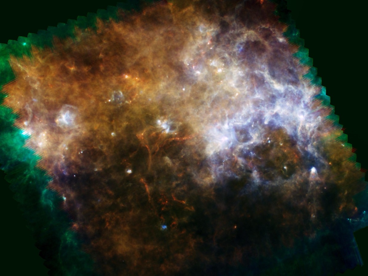 Nuages de poussière interstellaire orange, verts et bleus occupant tout le cadre, traversés de filaments et parsemés de points brillants