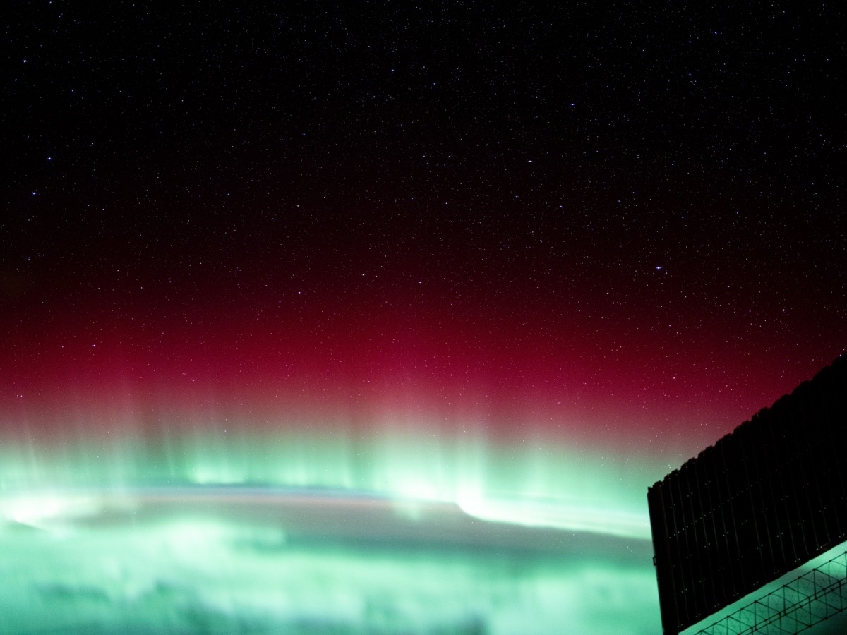 Aurore boréale rouge et verte photographiée depuis l'orbite terrestre, avec un panneau solaire de la Station spatiale au premier plan