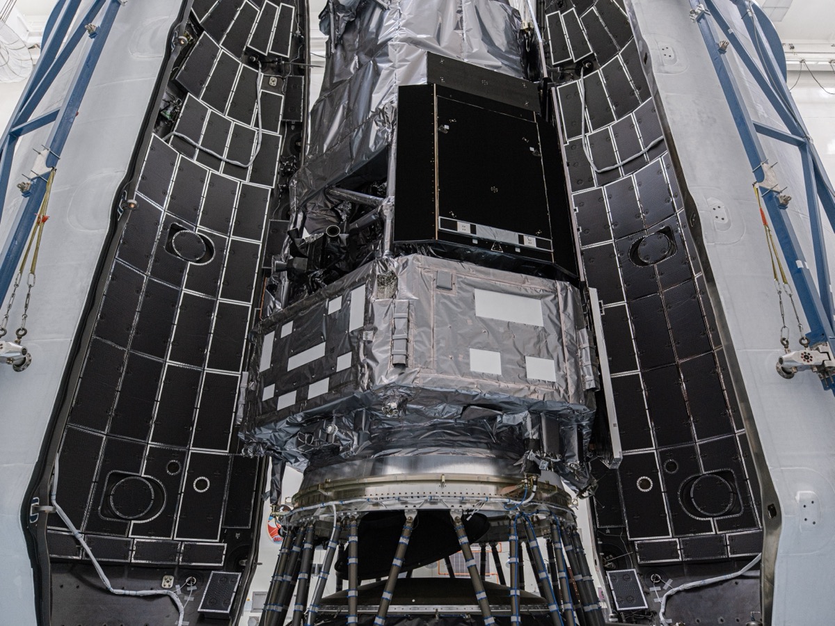 Le télescope spatial Nancy Grace Roman, emballé de couvertures isolantes argentées, placé entre les deux demi-coiffes noires d'une fusée Falcon Heavy dans un hall d'assemblage