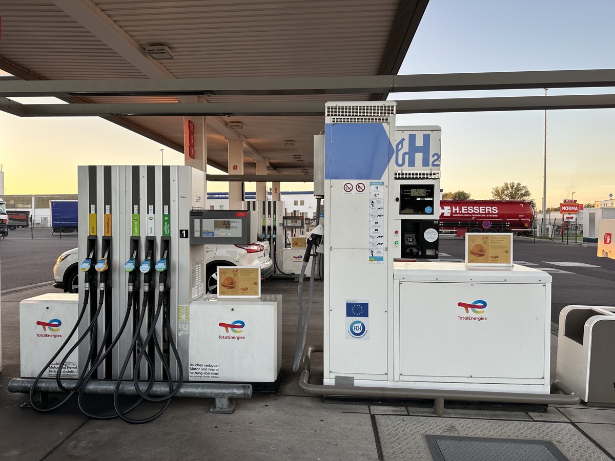 Distributeur d’hydrogène blanc marqué H2 installé à côté de pompes à carburant classiques, sous l’auvent d’une station-service TotalEnergies au lever du jour