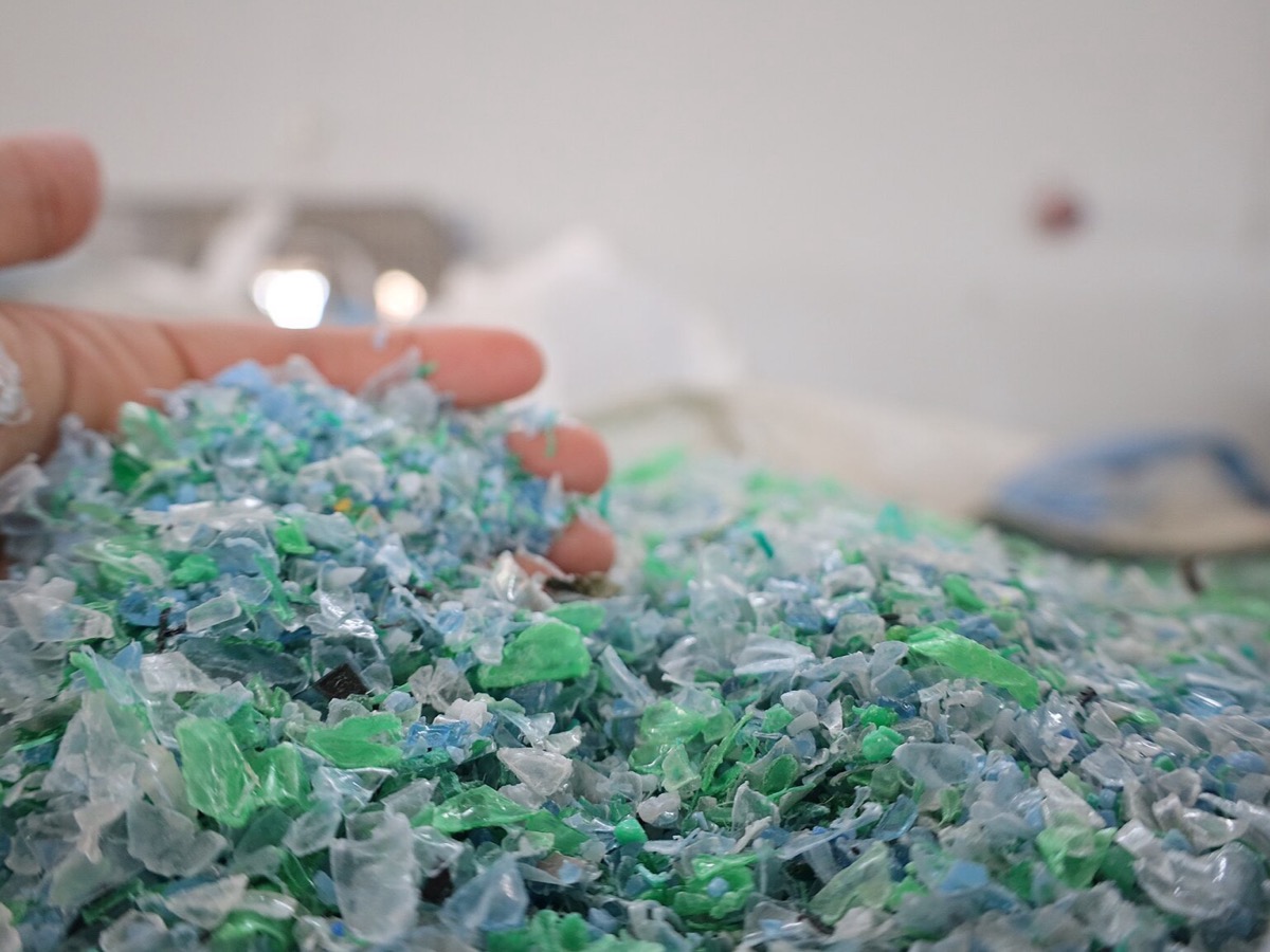 Main tenant une poignée de paillettes de plastique vertes, bleues et translucides au-dessus d'un tas, dans un atelier