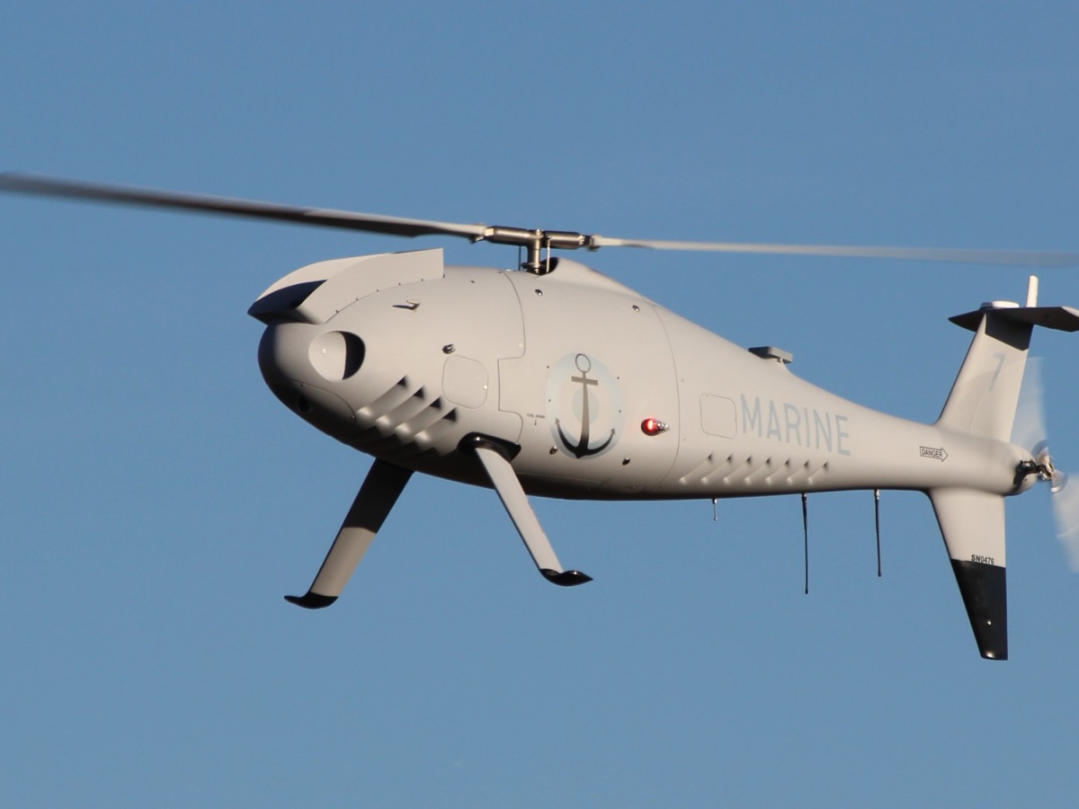 Drone hélicoptère gris clair portant une ancre de marine et l'inscription Marine, en vol sur fond de ciel bleu