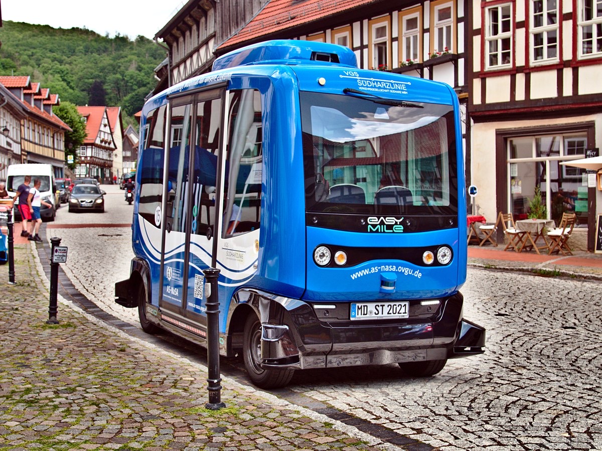 Navette électrique autonome bleue et blanche EasyMile EZ10 arrêtée sur une rue pavée bordée de maisons à colombages, dans une petite ville allemande