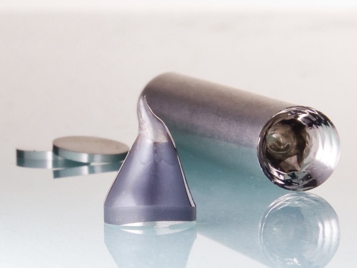 Cylindre et cône de métal gris brillant posés sur une surface réfléchissante, à côté de deux petits disques métalliques