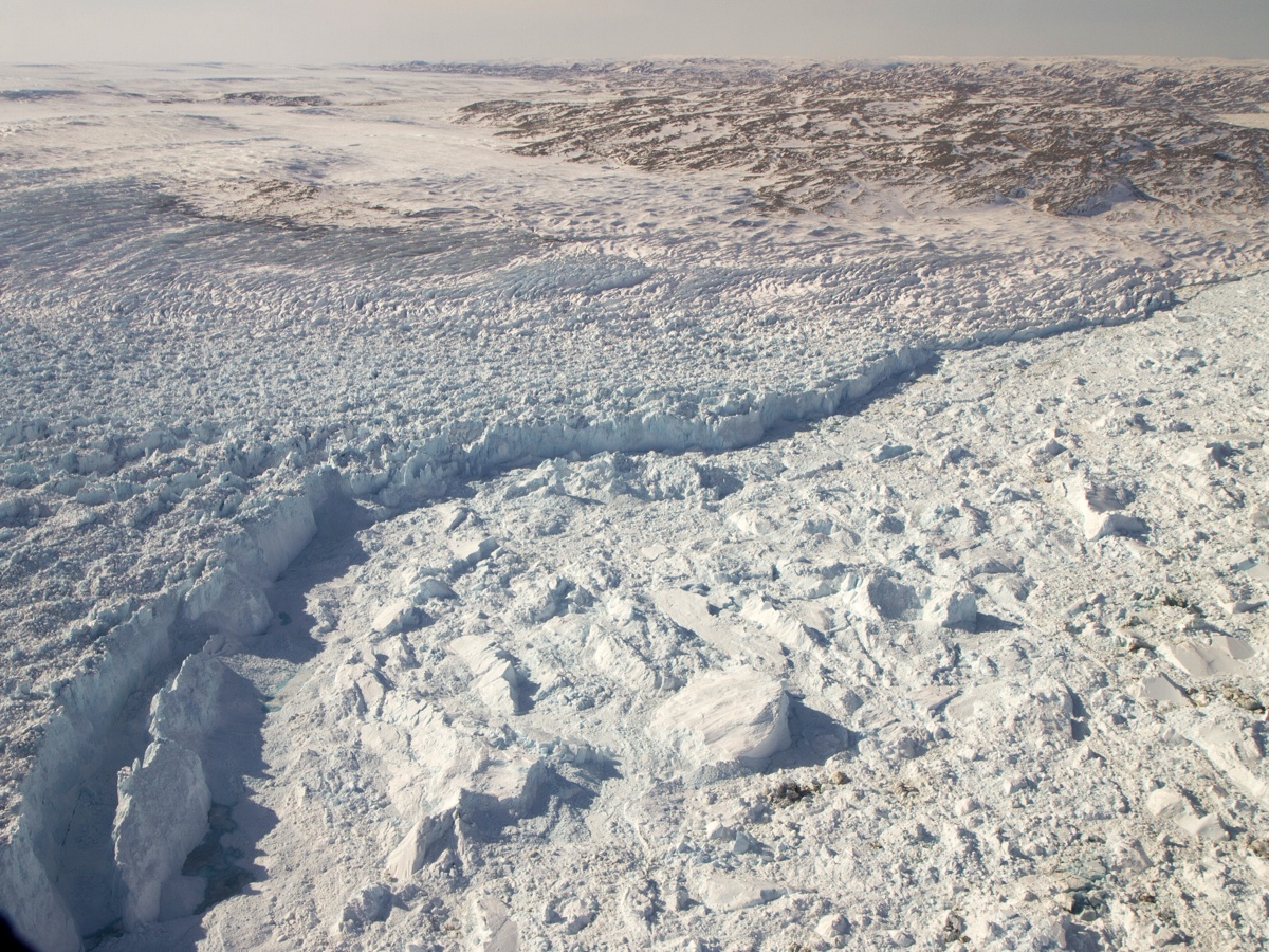 Front du glacier Jakobshavn au Groenland vu d'avion : une falaise de glace fracturée domine un chaos de blocs et d'icebergs