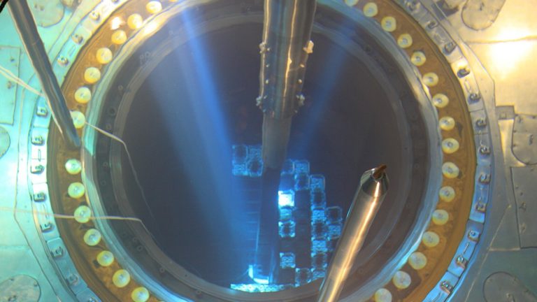 Vue plongeante dans la cuve ouverte d'un réacteur nucléaire pendant un arrêt, l'eau bleutée laissant apparaître le quadrillage des assemblages combustibles