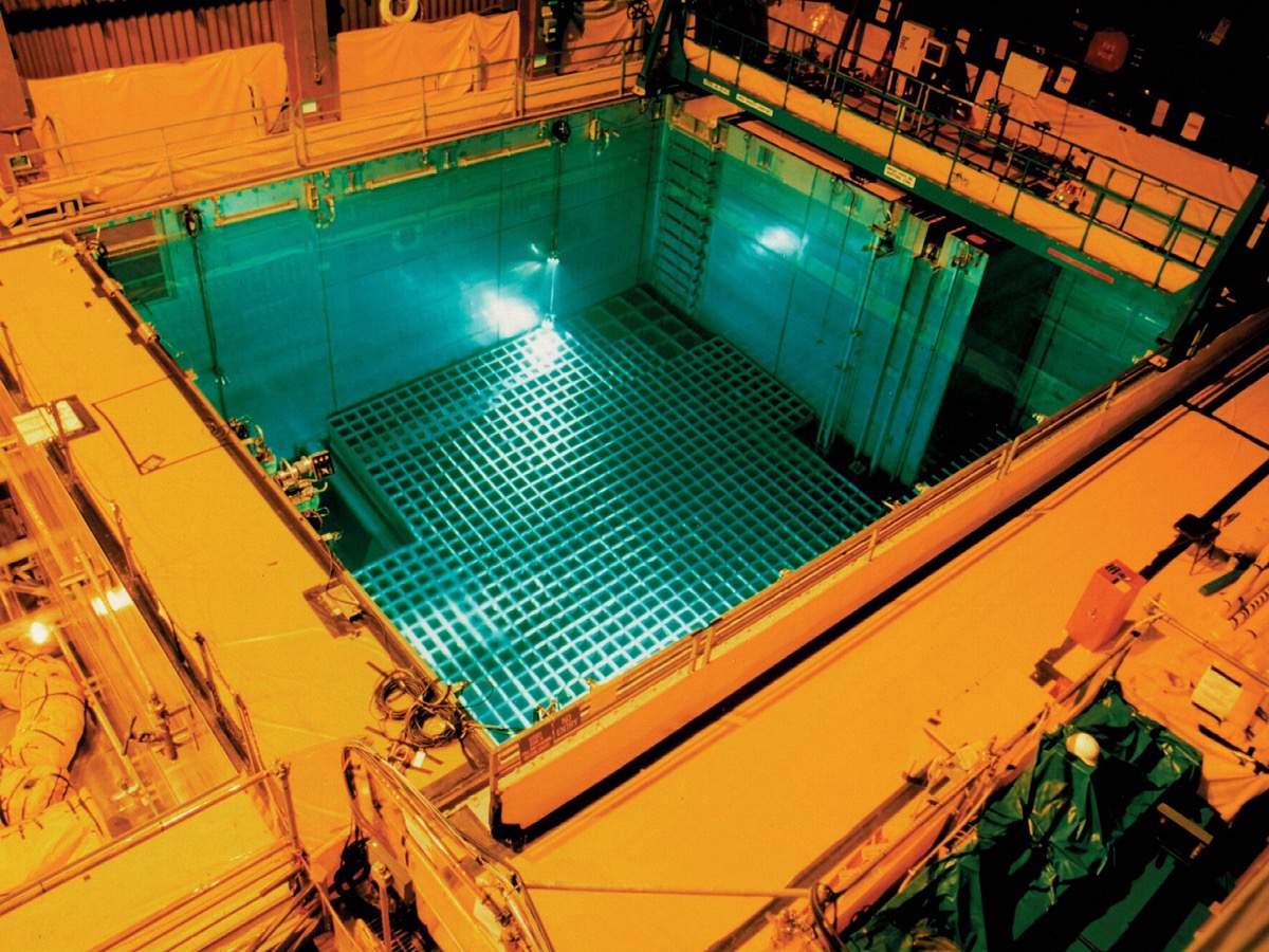 Vue plongeante sur une piscine d'entreposage remplie d'eau turquoise, avec un râtelier quadrillé posé au fond et des passerelles métalliques autour