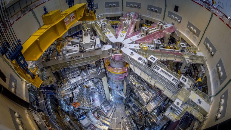 Vue plongeante du puits d'assemblage du tokamak ITER, avec les segments du vaisseau à vide, les portiques blancs et un pont roulant jaune