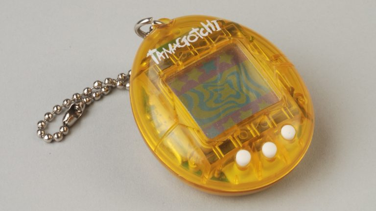 Tamagotchi jaune translucide de 1997 avec sa chaînette à billes, posé sur un fond gris