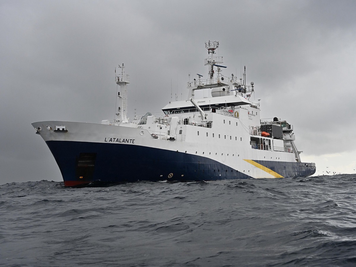 Le navire océanographique L'Atalante, coque bleue et superstructures blanches, vu de face par mer agitée sous un ciel gris