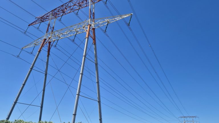 Deux pylônes à très haute tension supportant de nombreux câbles se détachant sur un ciel bleu sans nuage