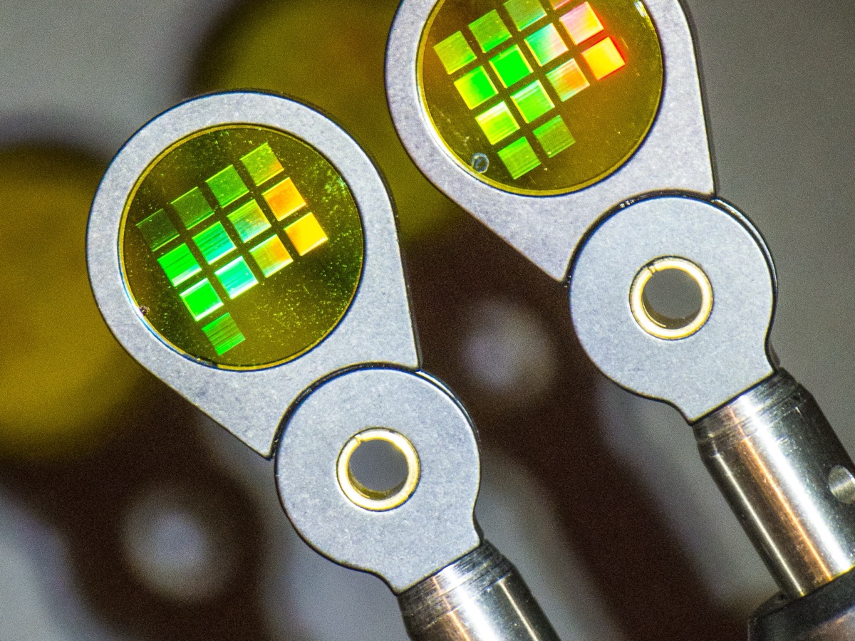 Deux petits disques optiques tenus par des pinces métalliques, couverts de carrés irisés verts et orangés produits par des réseaux de diffraction
