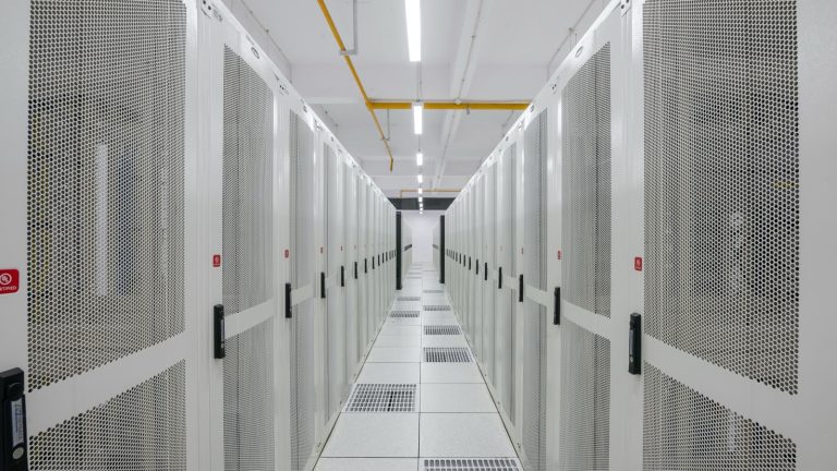 Allée froide d'un centre de données, bordée d'armoires de serveurs blanches perforées, sur un plancher technique