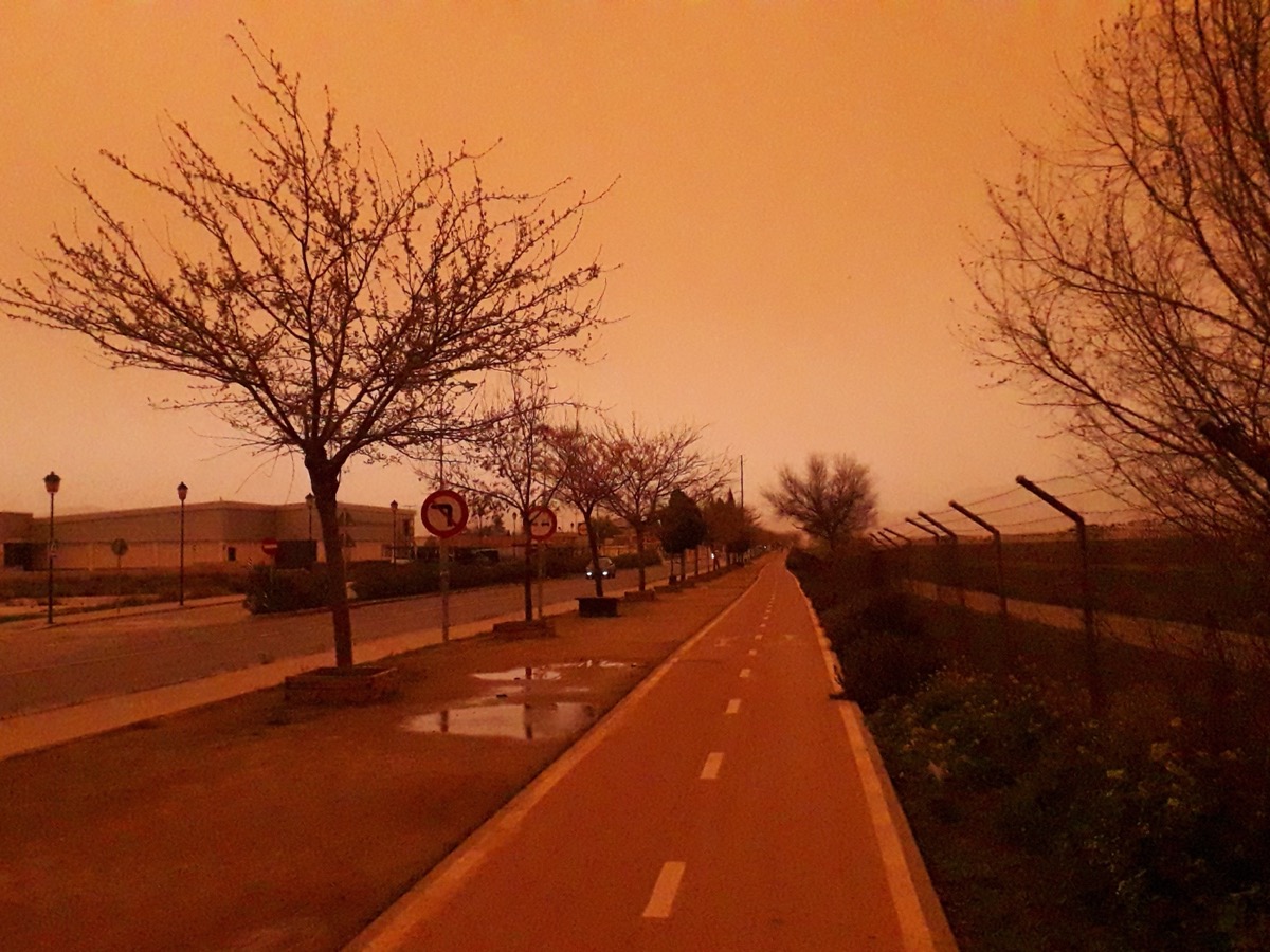 Ciel orange et route déserte pendant un épisode de poussière saharienne dans la plaine de Grenade, en Espagne