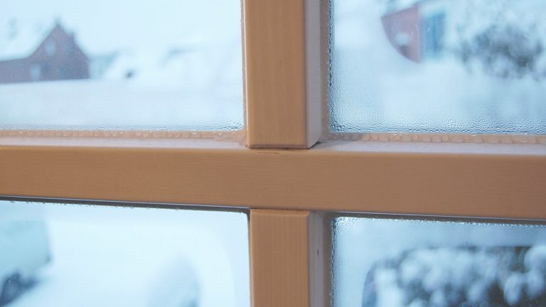 Gouttelettes de condensation sur les carreaux intérieurs d’une fenêtre à petits bois, devant un paysage enneigé