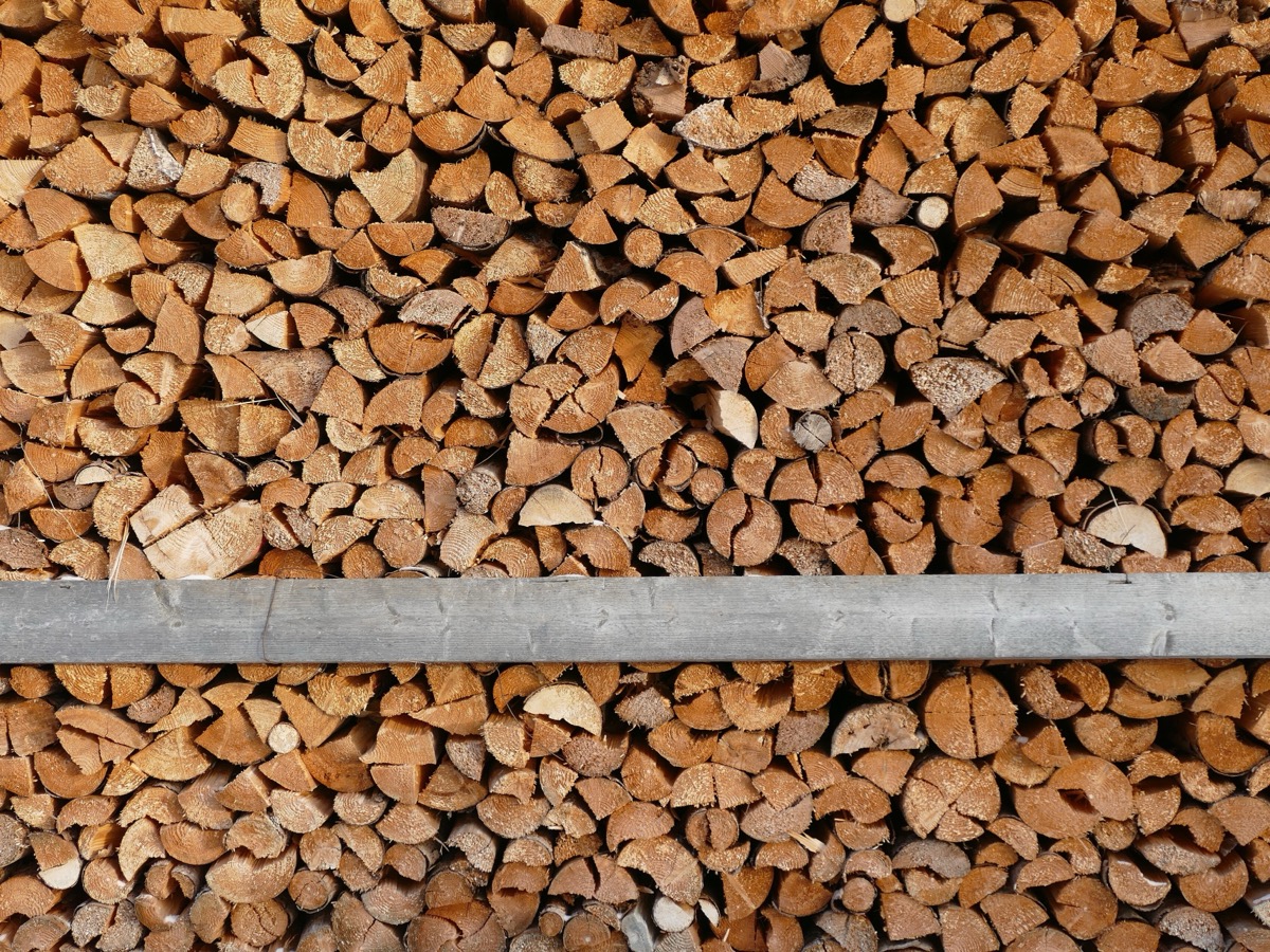 Bûches de bois de chauffage fendues en quartiers, empilées serré sur deux rangées séparées par une planche horizontale grise, sections claires tournées vers l'objectif