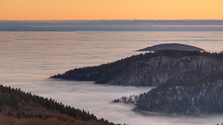 Vallée entièrement remplie de brouillard au coucher du soleil, avec des crêtes boisées émergeant de la nappe blanche
