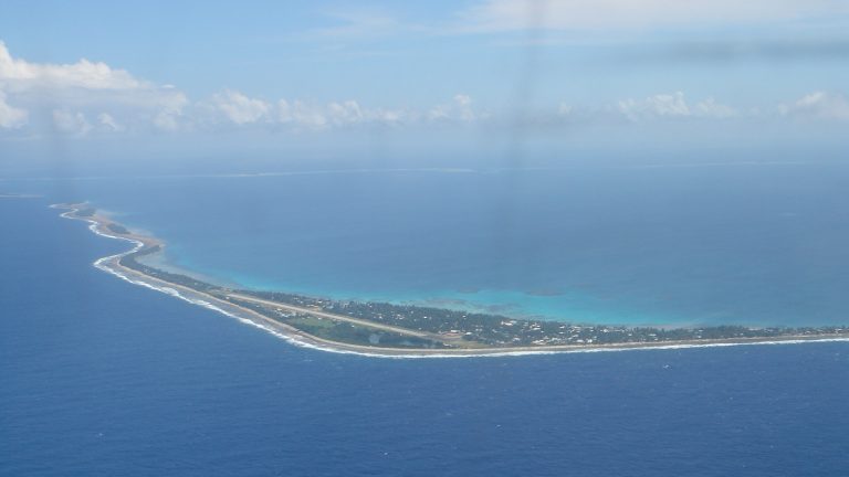 Vue aérienne d'un atoll très bas et allongé, bordé d'un lagon clair et entouré par l'océan