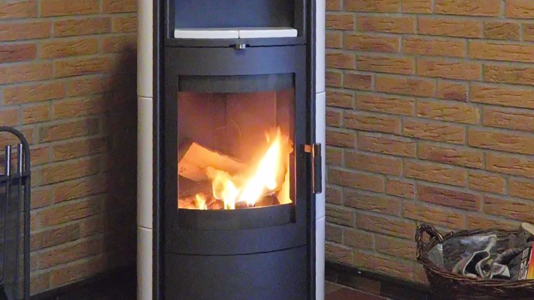 Poêle à bois noir et blanc en fonctionnement dans l'angle d'une pièce aux murs de briques, des flammes visibles derrière la vitre