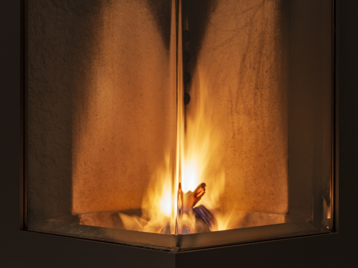 Petites flammes jaunes derrière la vitre d'angle d'un poêle à bois, dans une chambre de combustion aux parois claires