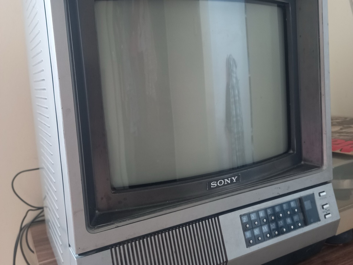 Téléviseur cathodique Sony à façade argentée, écran bombé éteint et clavier de réglage sous l’écran, posé sur un meuble en bois