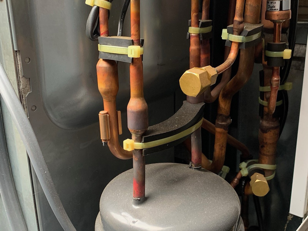 Vue de l'intérieur d'une unité extérieure de pompe à chaleur, avec le compresseur cylindrique et les tubes de cuivre du circuit frigorifique