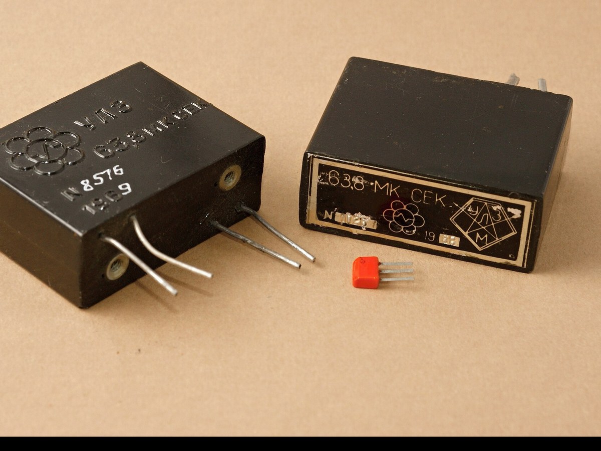 Deux boîtiers noirs de lignes à retard ultrasonores marqués 63,8 microsecondes, posés sur un fond uni à côté d'un petit composant orange