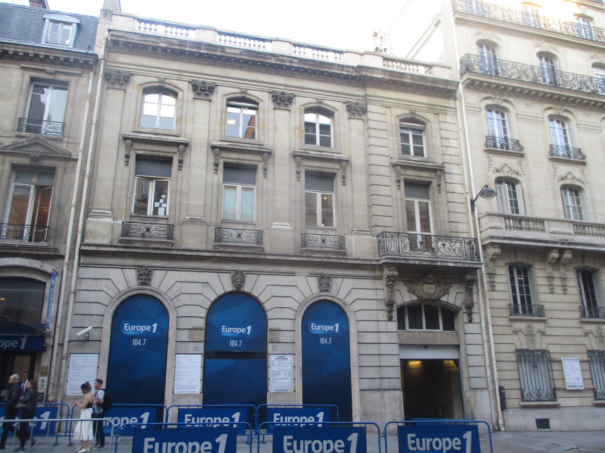 Façade en pierre de taille du 26 bis rue François-Ier à Paris, avec trois grandes baies cintrées habillées de bleu au rez-de-chaussée et des barrières sur le trottoir
