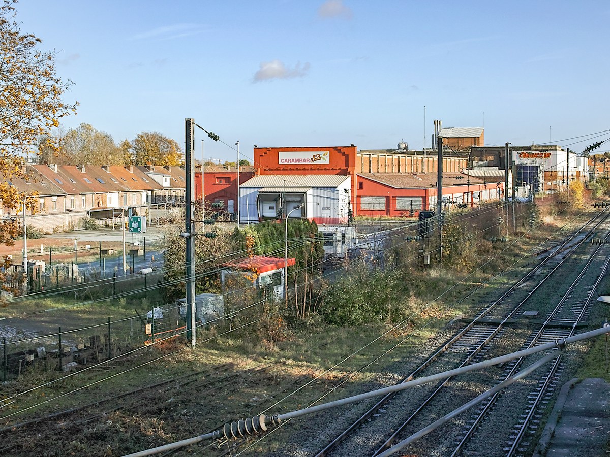 Usine de confiserie aux bâtiments rouges à Marcq-en-Barœul vue depuis un pont, avec des maisons de brique à gauche et des voies ferrées au premier plan