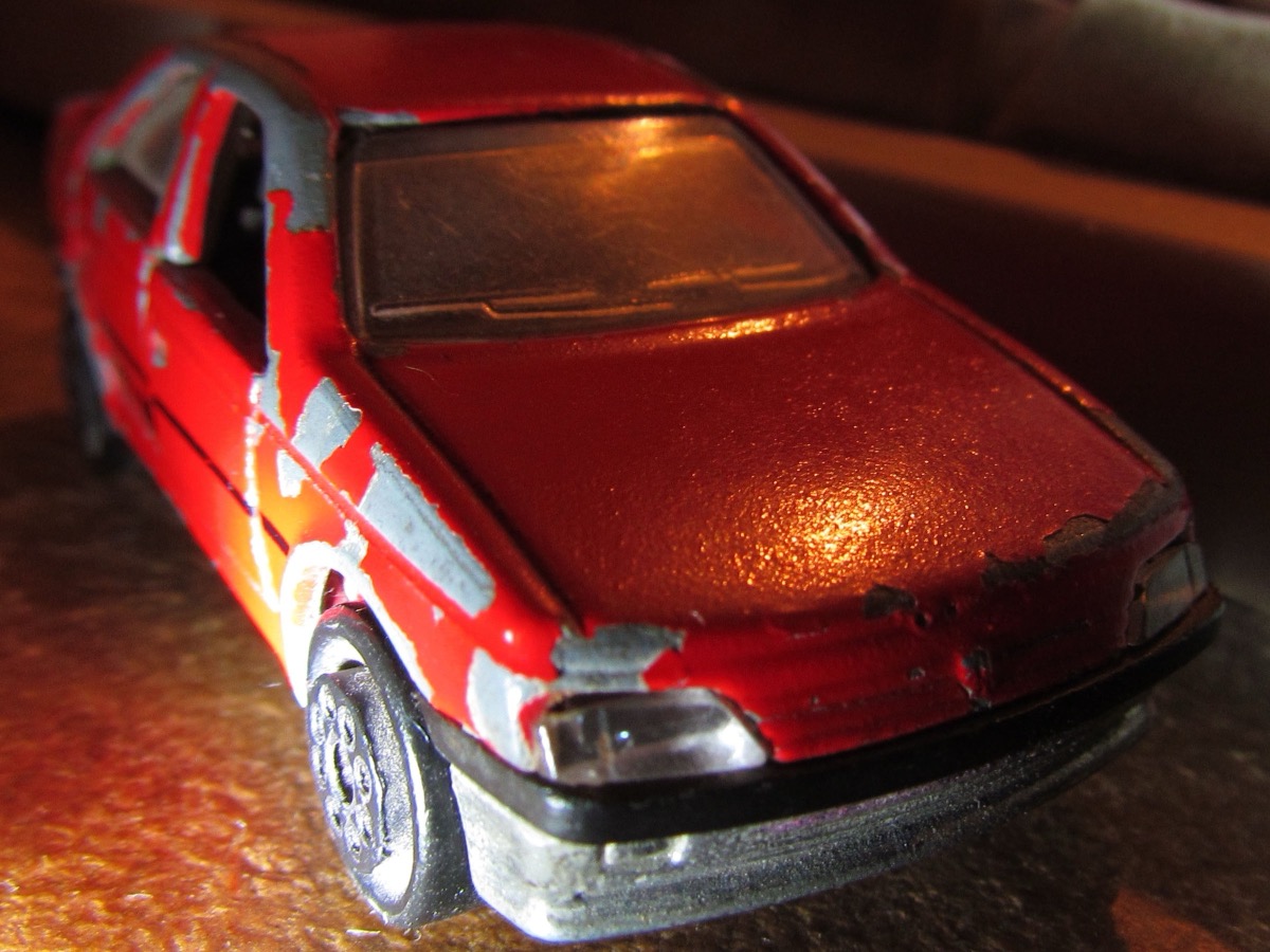 Miniature Majorette de Peugeot 405 rouge vue de trois quarts avant, peinture écaillée laissant voir le métal gris sur les portières et le capot