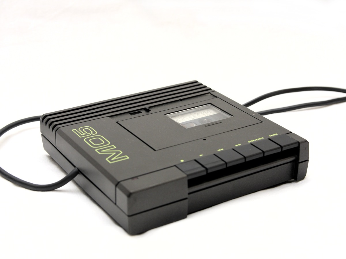 Lecteur-enregistreur de cassettes noir du Thomson MO5, avec ses touches de commande et son câble, posé sur un fond blanc