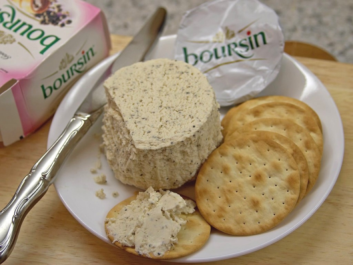 Fromage frais Boursin à l’ail et aux fines herbes posé dans une assiette avec des crackers, un couteau et son emballage