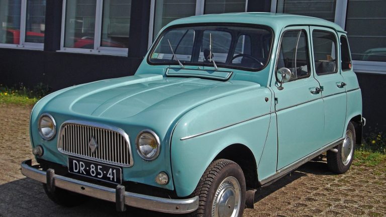 Renault 4L bleu clair de 1963 vue de trois quarts avant, garée sur des pavés devant la façade vitrée d’un bâtiment