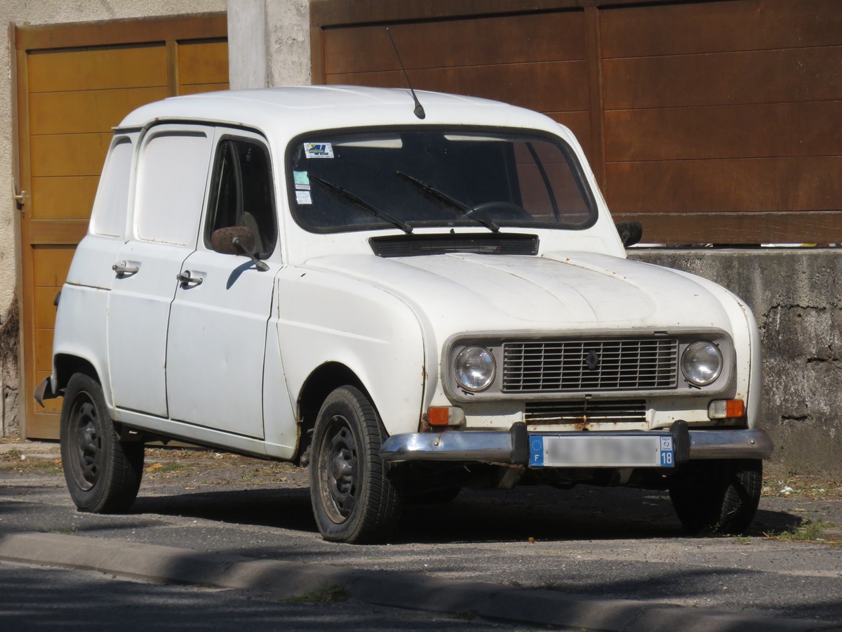 Renault 4 blanche garée le long d’un trottoir devant un portail en bois, carrosserie marquée par la rouille et calandre chromée
