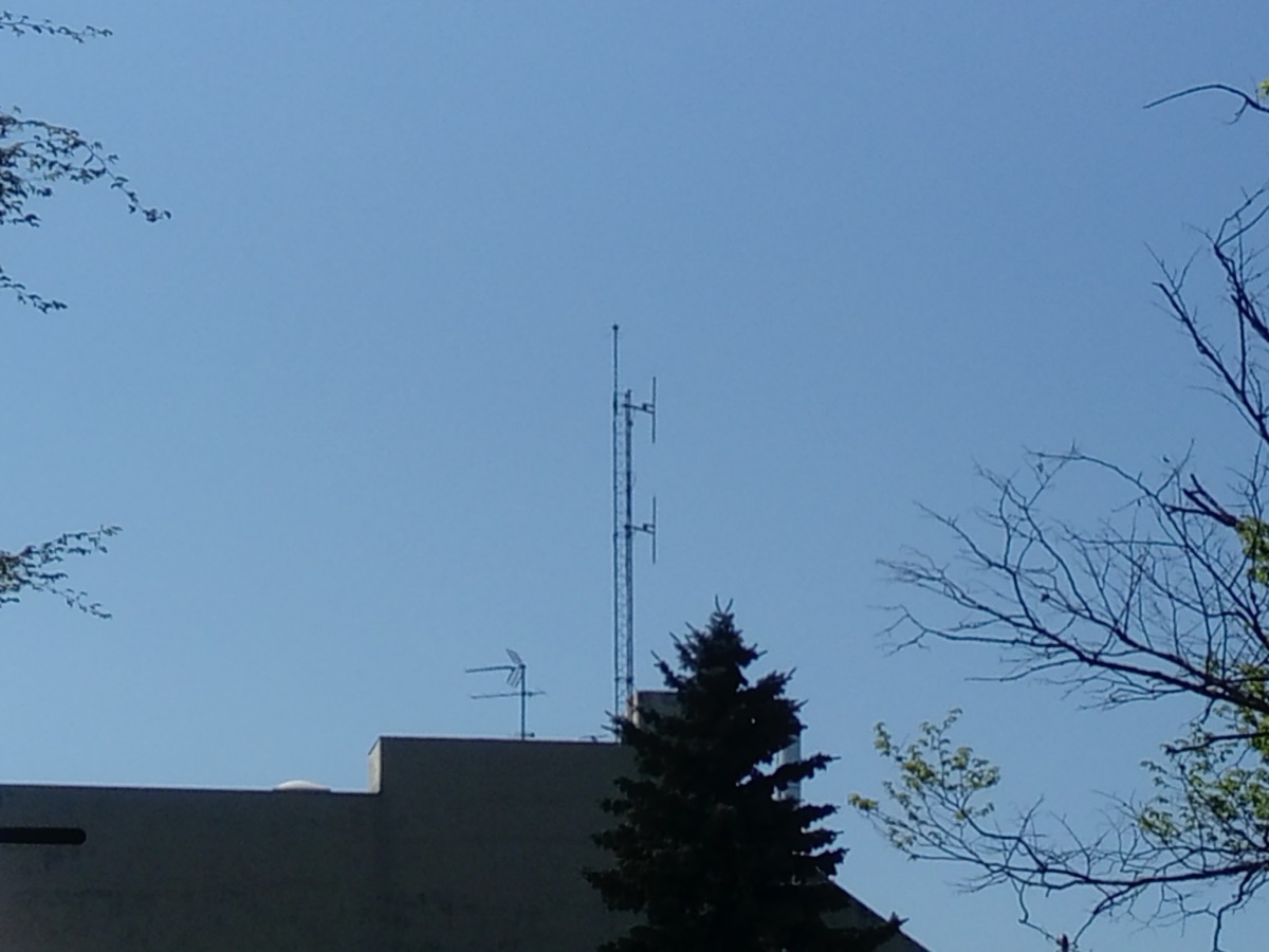 Mât d'antennes de radiodiffusion installé sur le toit plat d'un bâtiment, entouré d'arbres, sous un ciel dégagé