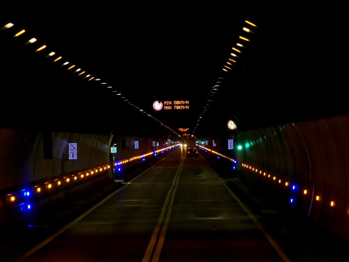 Intérieur du tunnel du Mont-Blanc de nuit, galerie unique à deux voies opposées séparées par une ligne jaune, bordée de plots lumineux