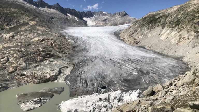 Langue du glacier du Rhône en Valais avec des bâches blanches posées sur le front, au bord du lac glaciaire