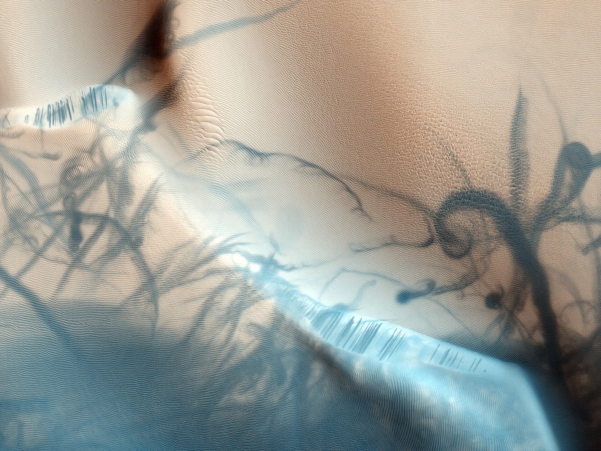 Vue orbitale de dunes martiennes claires striées de traînées sombres sinueuses laissées par des tourbillons de poussière
