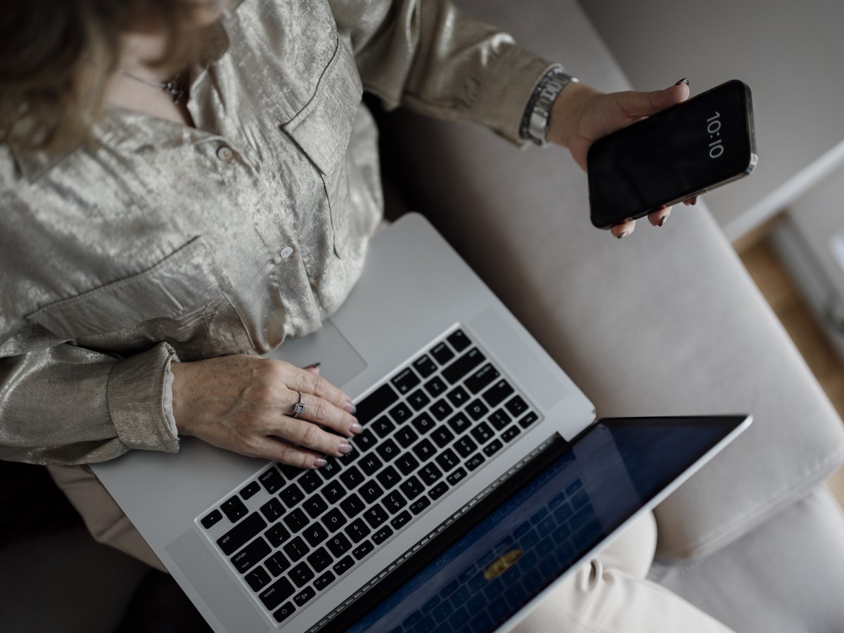 Vue de dessus d'une personne assise sur un canapé, tapant sur un ordinateur portable et tenant un téléphone dans l'autre main