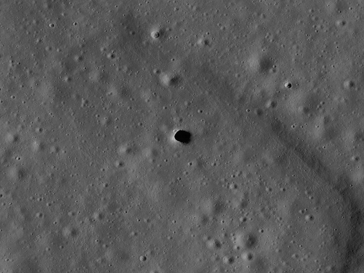 Trou sombre et ovale ouvert dans une plaine lunaire grise criblée de petits cratères
