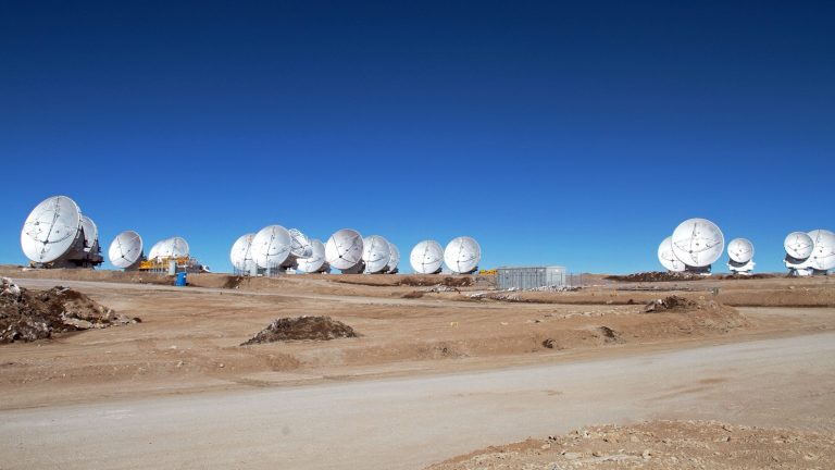 Rangée d'antennes paraboliques blanches posées sur un plateau désertique sous un ciel bleu profond