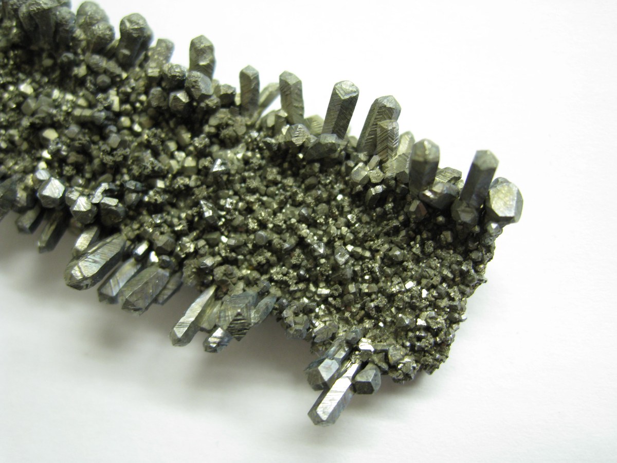 Barreau de cristaux de niobium métallique aux facettes grises posé sur un fond clair