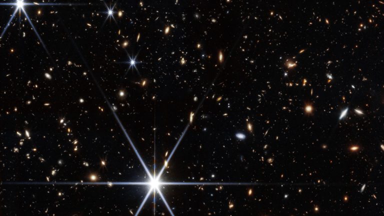 Champ profond rempli de petites galaxies de toutes formes sur le noir de l'espace, avec quelques étoiles brillantes à aigrettes de diffraction