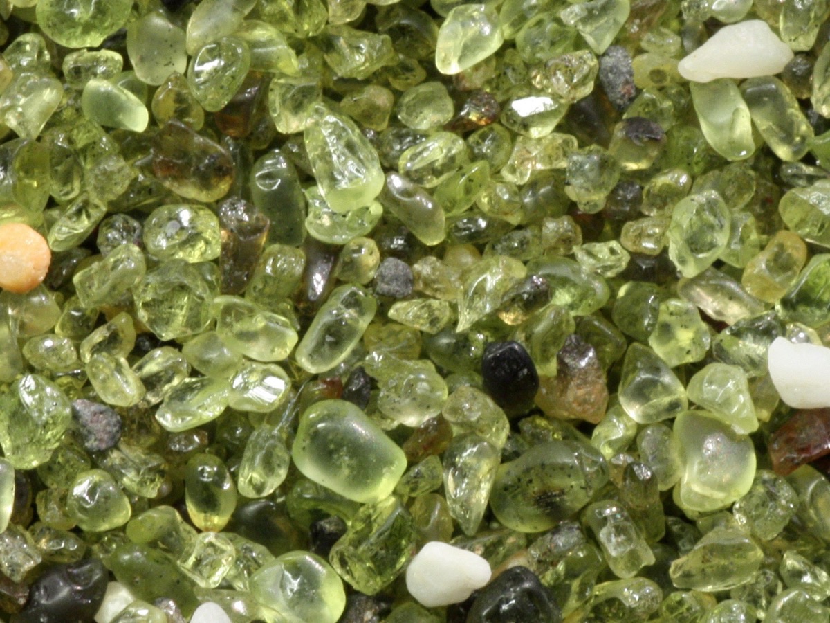 Gros plan sur des grains de sable vert translucides mêlés à quelques grains blancs et noirs