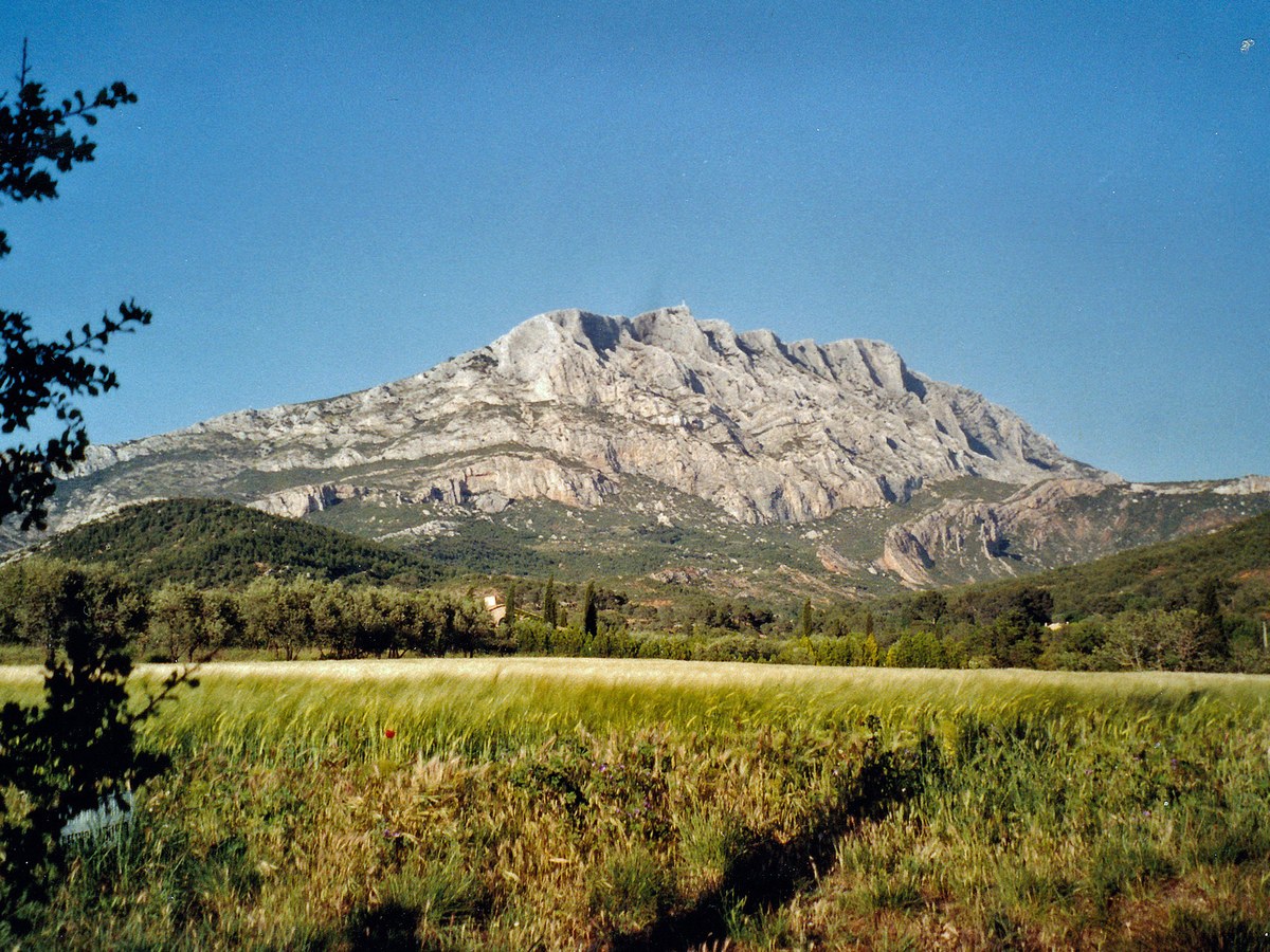 Massif calcaire clair de la montagne Sainte-Victoire dominant une plaine herbeuse sous un ciel bleu