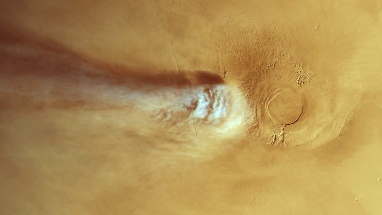 Vue depuis l'orbite d'une portion de la surface de Mars, avec un volcan à droite et une longue traînée de nuage blanc étirée vers la gauche